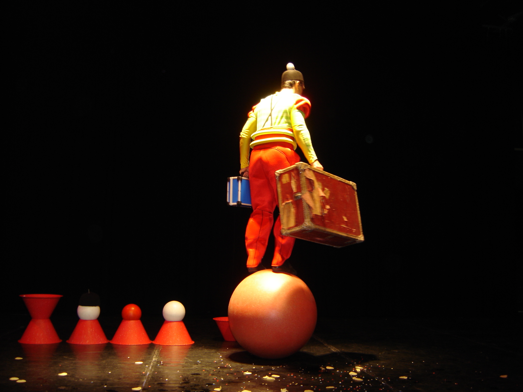 Un clown avec deux valises qui part en équilibre sur une boule Cirkonflex
